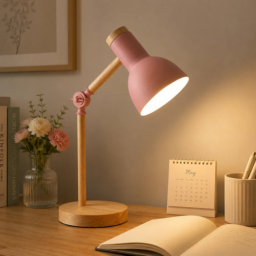 Pink adjustable desk lamp lit on a wooden desk