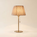 Alma table lamp with a pleated oatmeal shade on a slender brushed brass stem, front view