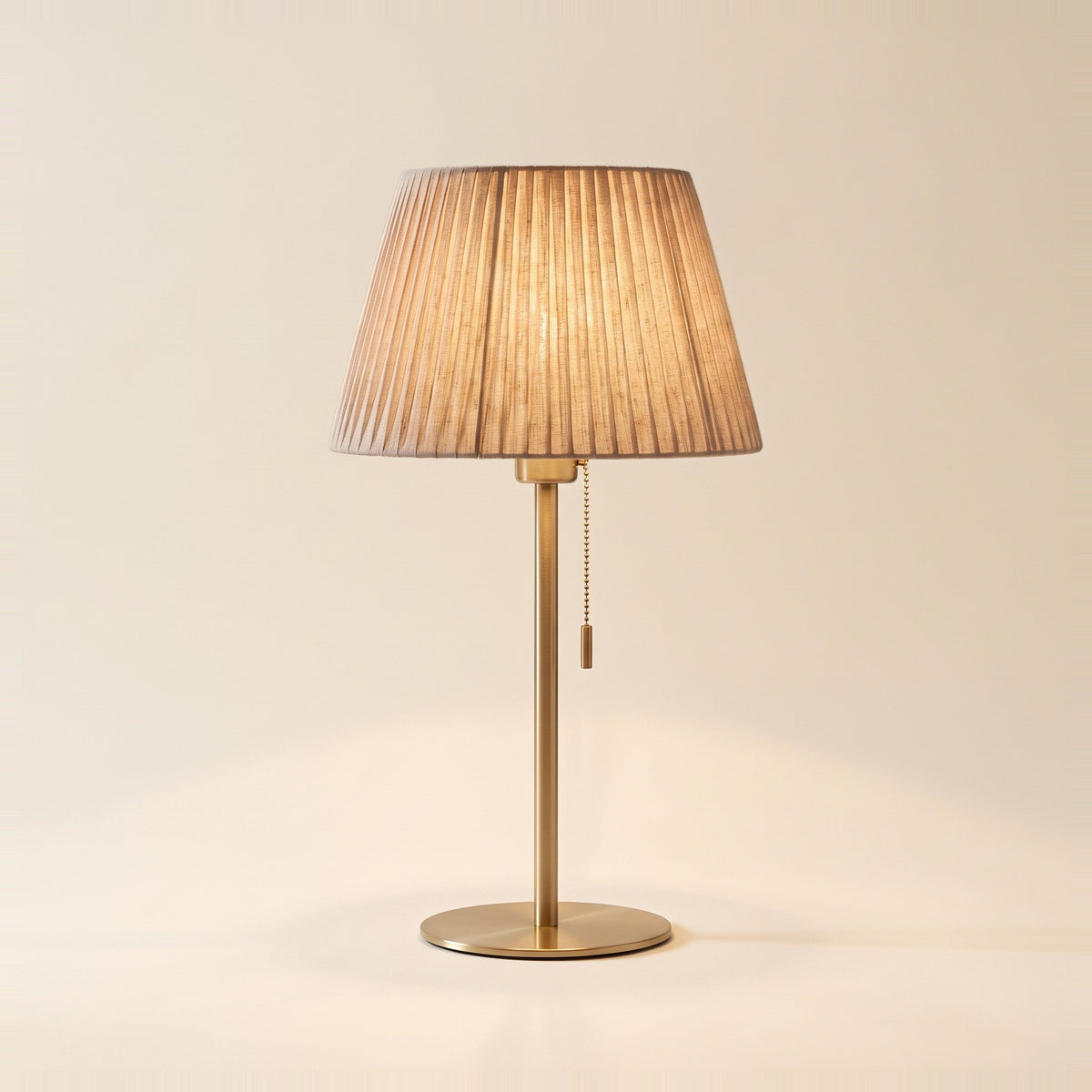 Alma table lamp with a pleated oatmeal shade on a slender brushed brass stem, front view