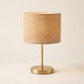 Alva table lamp with a natural jute drum shade on a brushed brass base, front view