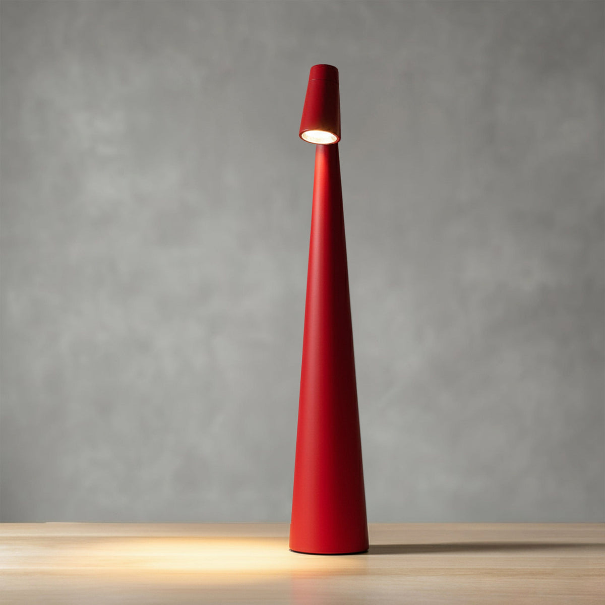 Bexley table lamp in red, lit against a grey wall