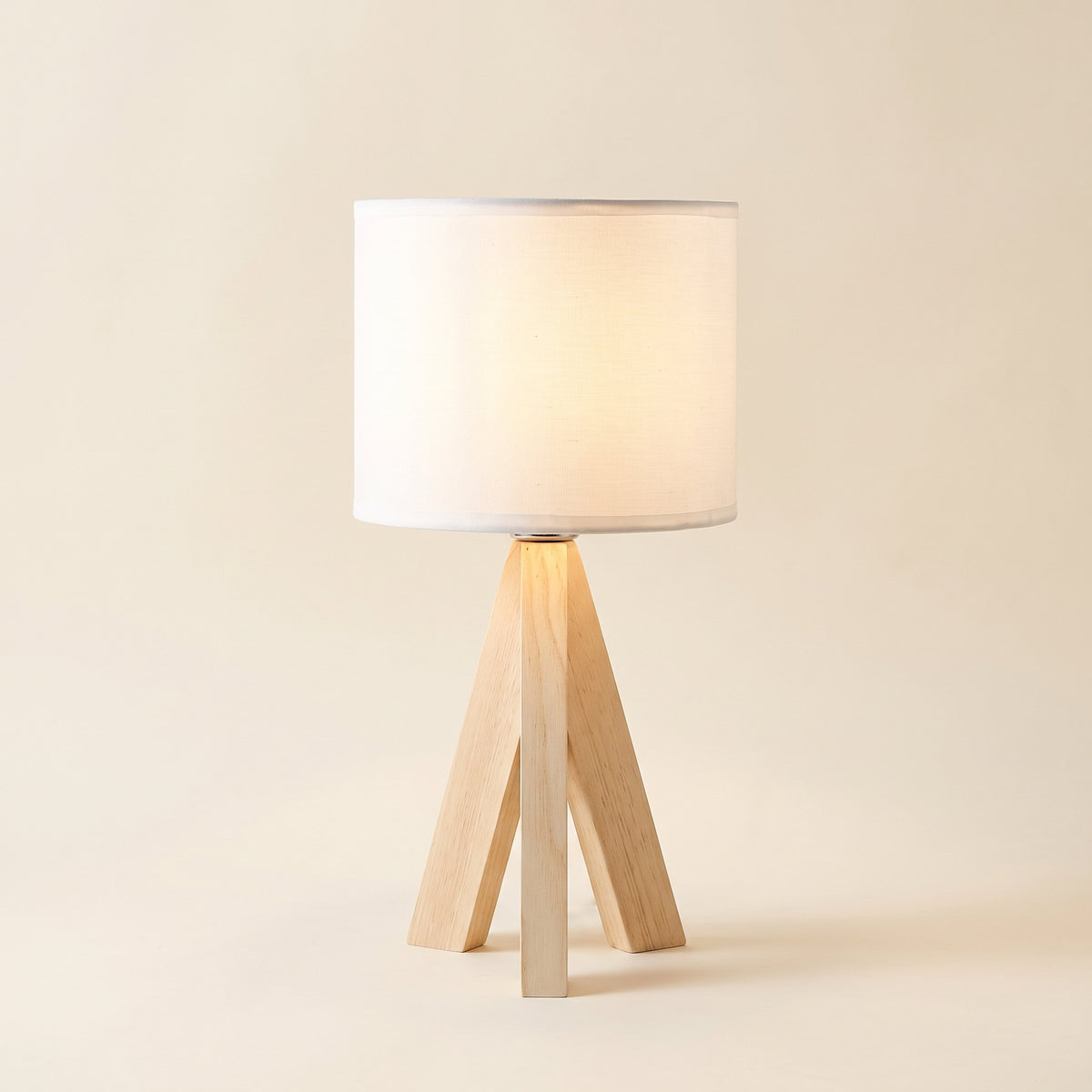 Birk table lamp with a solid wood tripod base and white drum shade, lit, on a cream background, Style Room