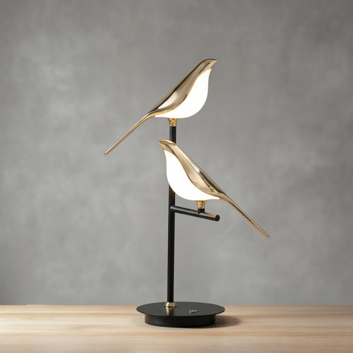 Cora bird table lamp unlit against a grey wall, two gold birds on a slim black post