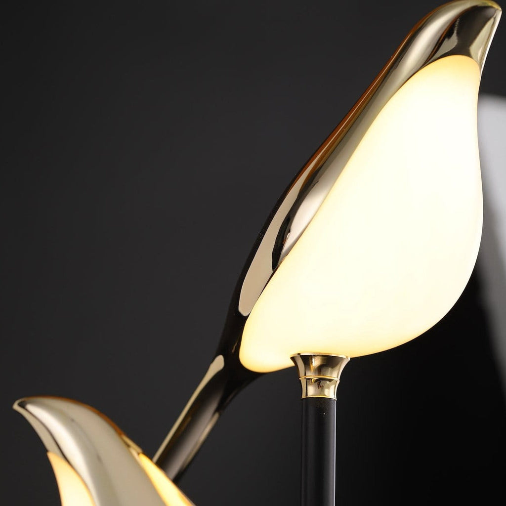 Close-up of the Cora lamp, showing the polished gold bird body and the white glowing underside