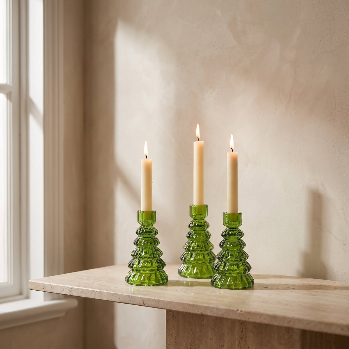 Cresta green glass candle holders with lit taper candles on a travertine console