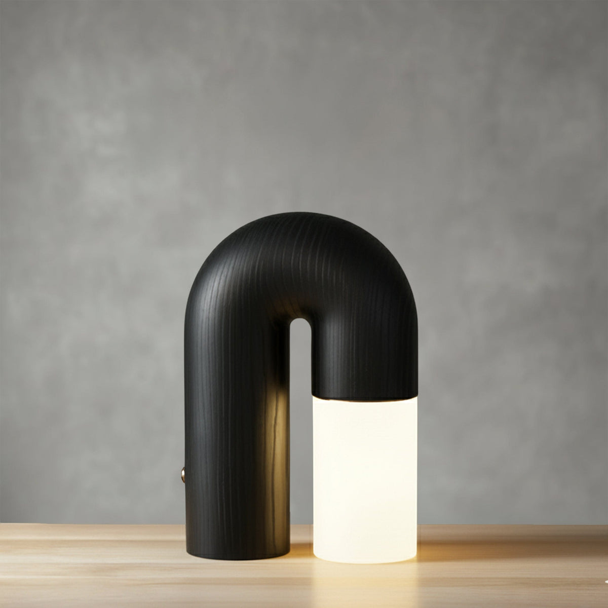 Diora table lamp in natural oak, lit on a wooden surface against a grey wall