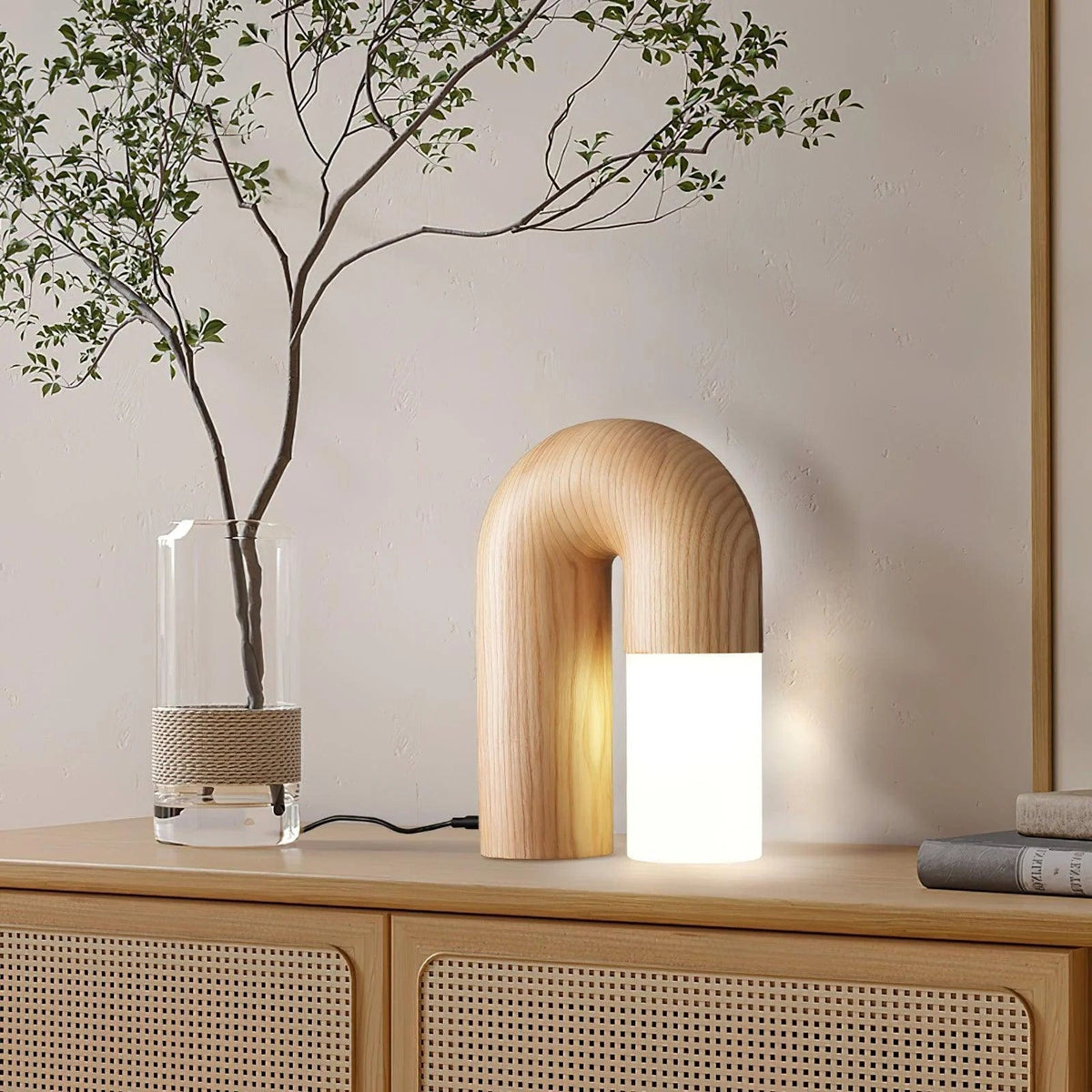 Diora table lamp lit on a rattan sideboard beside a glass vase with branches