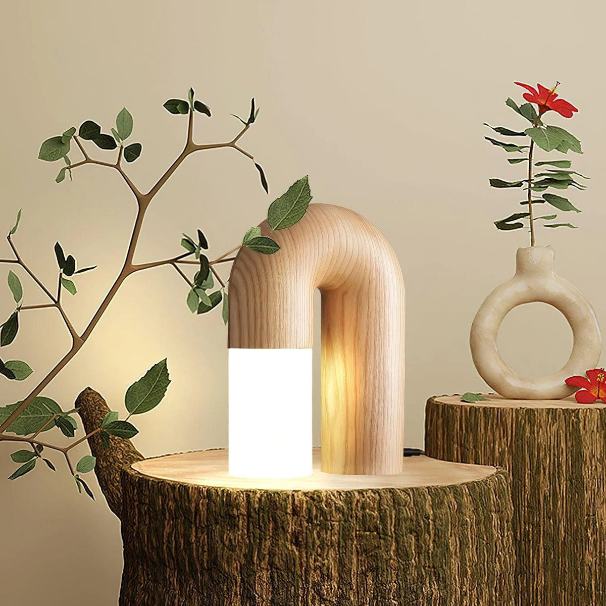 Diora table lamp lit on a tree stump beside a ceramic vase and a red flower
