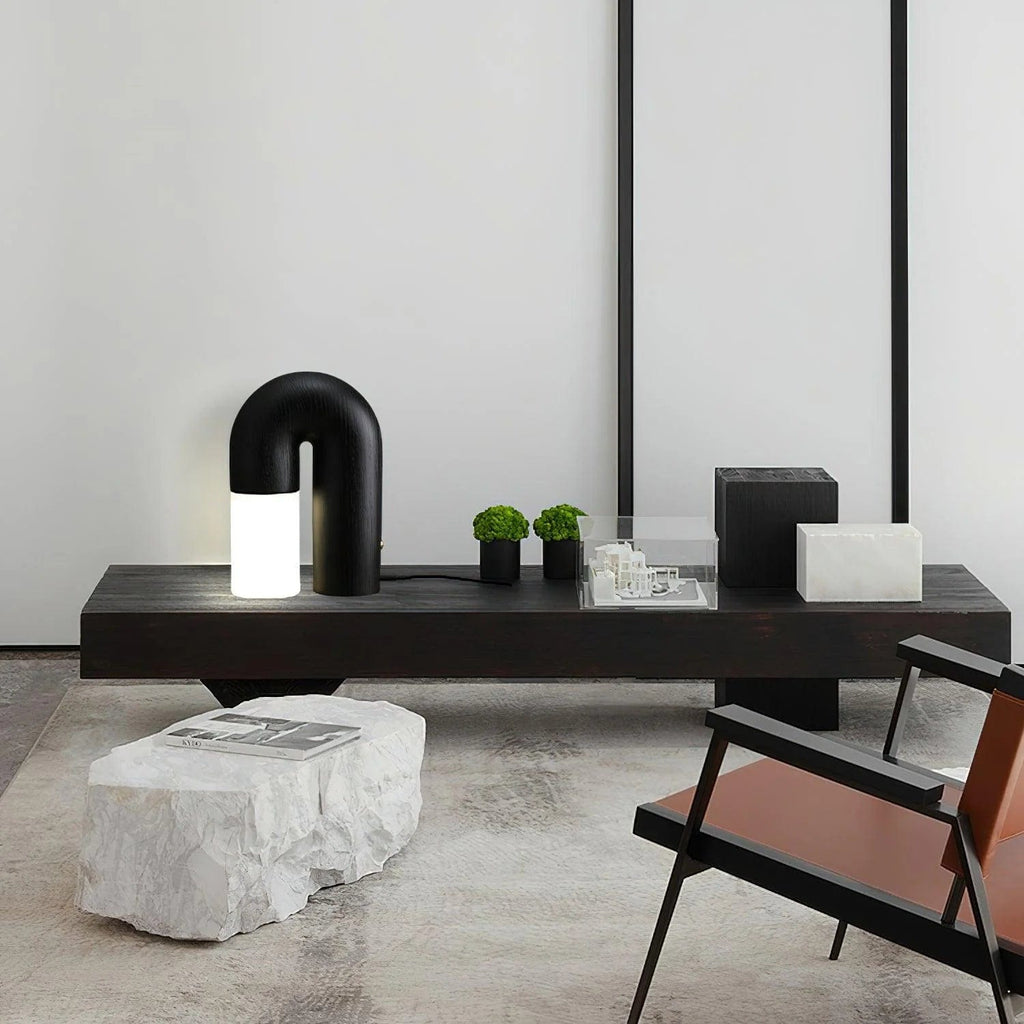 Diora table lamp in black finish, lit on a dark bench in a minimalist room