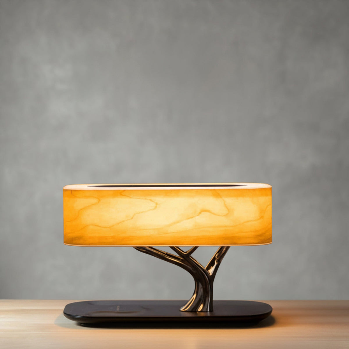 Liora table lamp lit against a grey wall, oval wood-veneer shade on a chrome branch stem