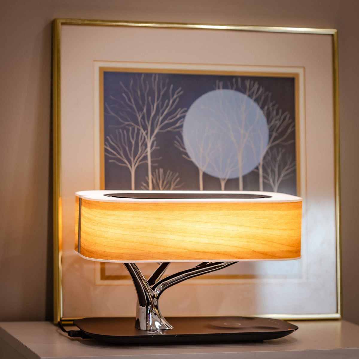 Liora table lamp lit in front of a framed print of winter trees