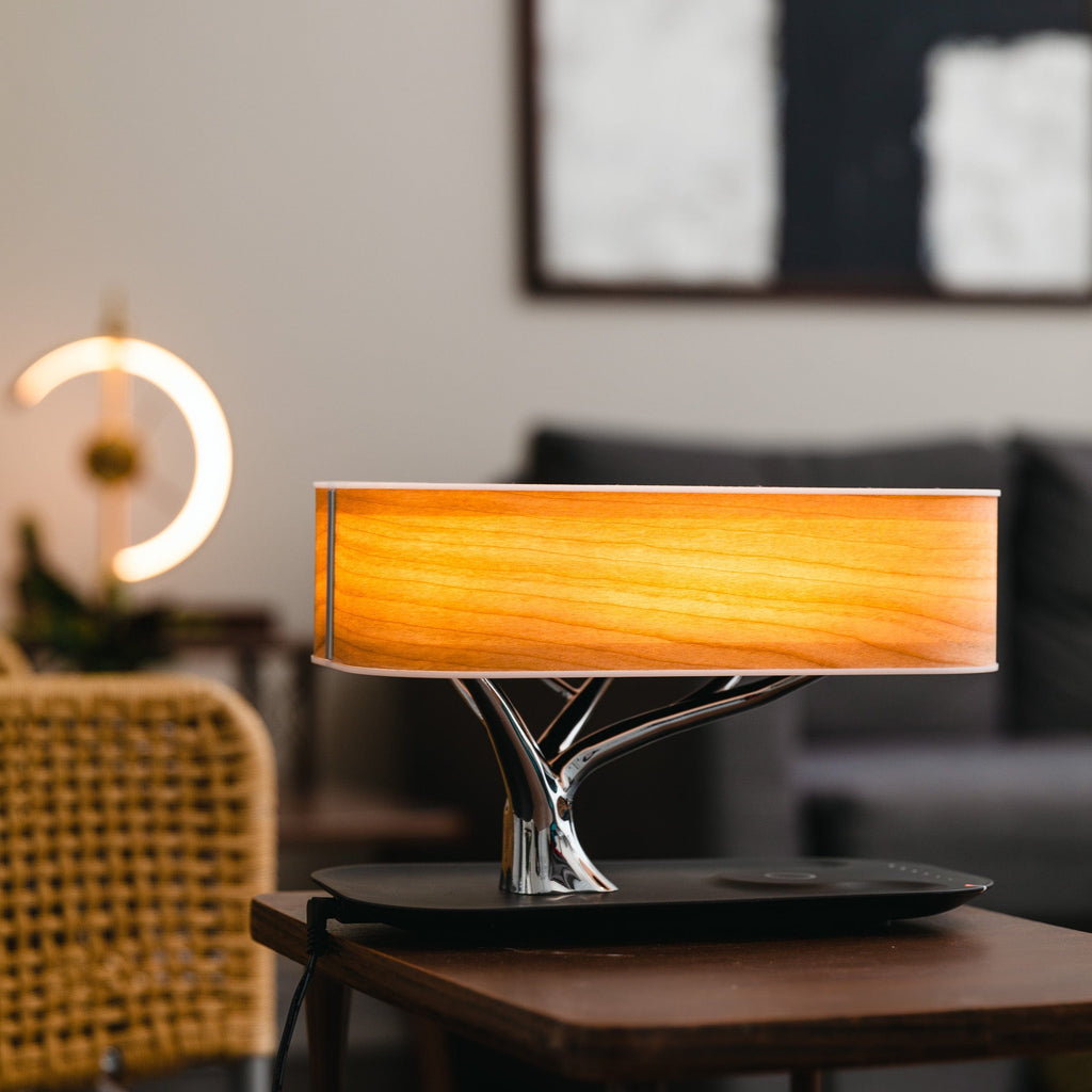 Liora table lamp lit on a side table in a living room with a sofa behind