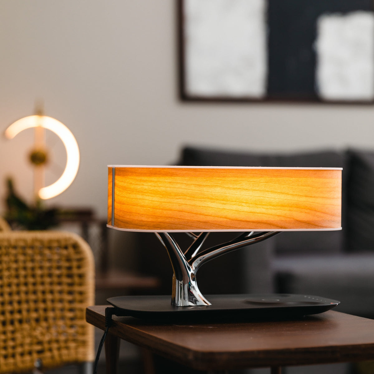Liora table lamp lit on a side table in a living room with a sofa behind