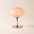 Lolly cordless table lamp with a pink glass dome, lit, on a cream background, Style Room