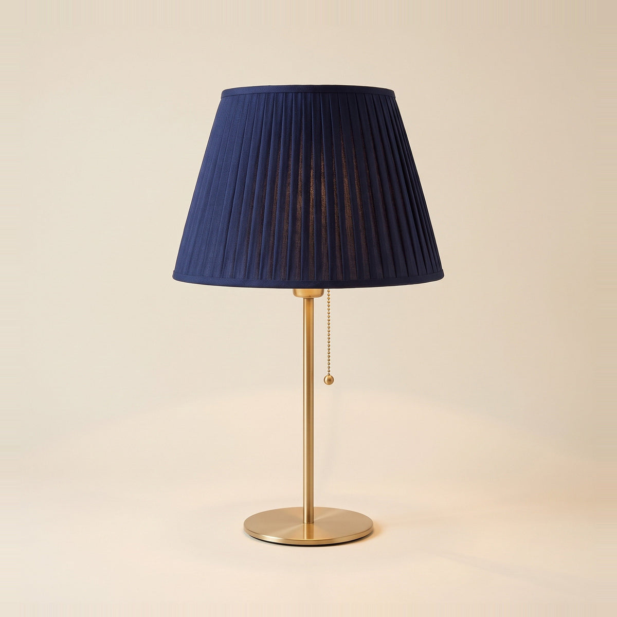 Neve table lamp with a navy pleated shade on a brushed brass stem, front view