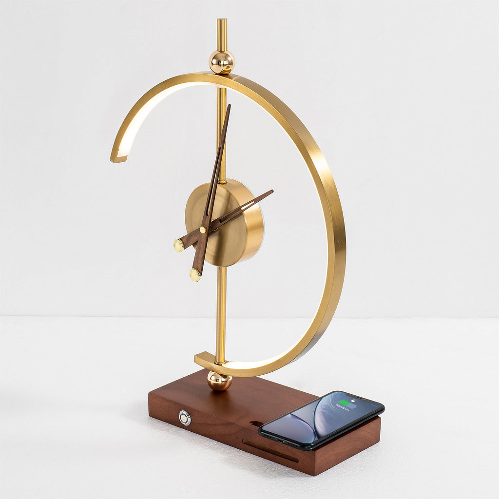 Orin clock lamp unlit, brass arc and analogue clock on a walnut base with a phone charging flat on the pad