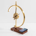 Orin clock lamp unlit, brass arc and analogue clock on a walnut base with a phone charging flat on the pad