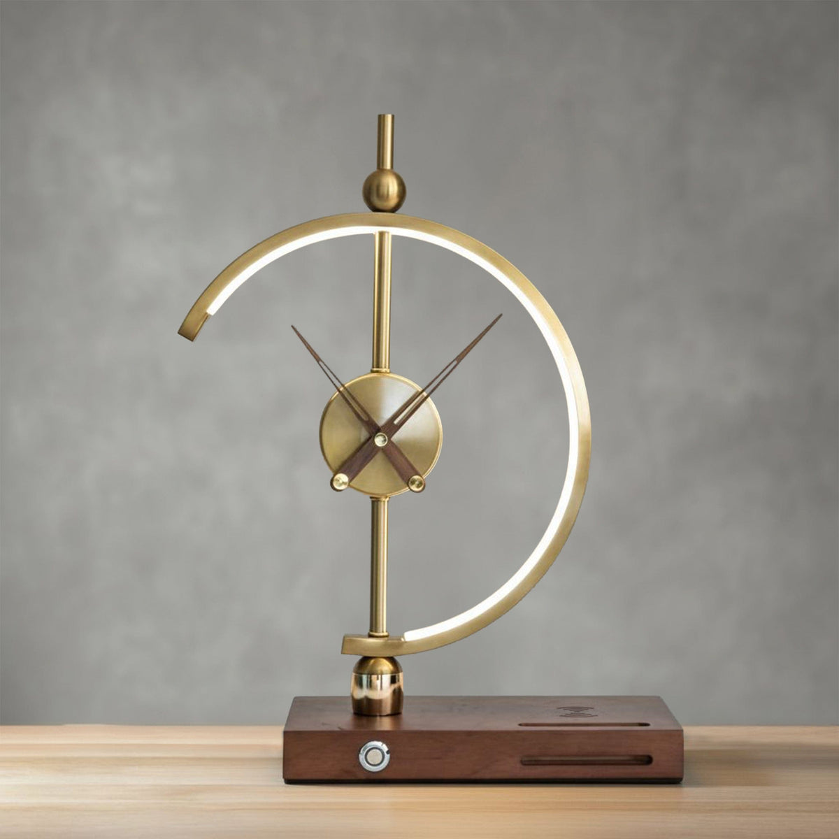 Orin clock lamp lit against a grey wall, warm glow along the inner edge of the brass arc
