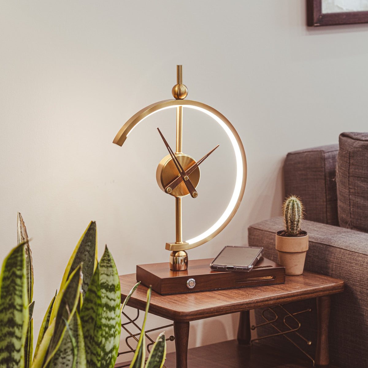 Orin clock lamp lit on a wooden side table beside a sofa in a living room