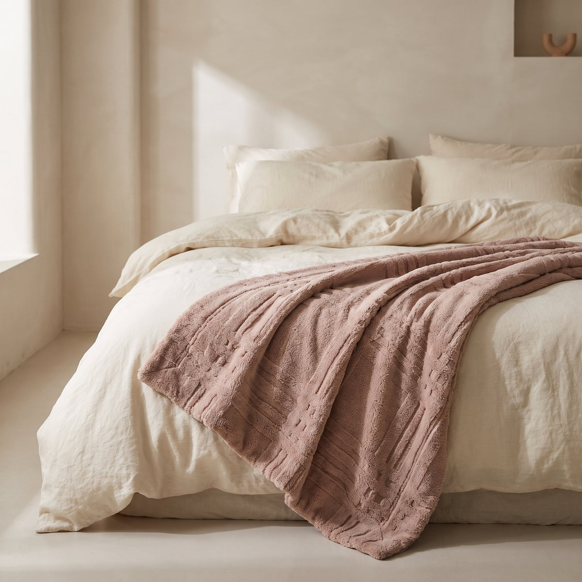 Pavo dusty pink embossed grid blanket draped across a bed dressed in cream linen