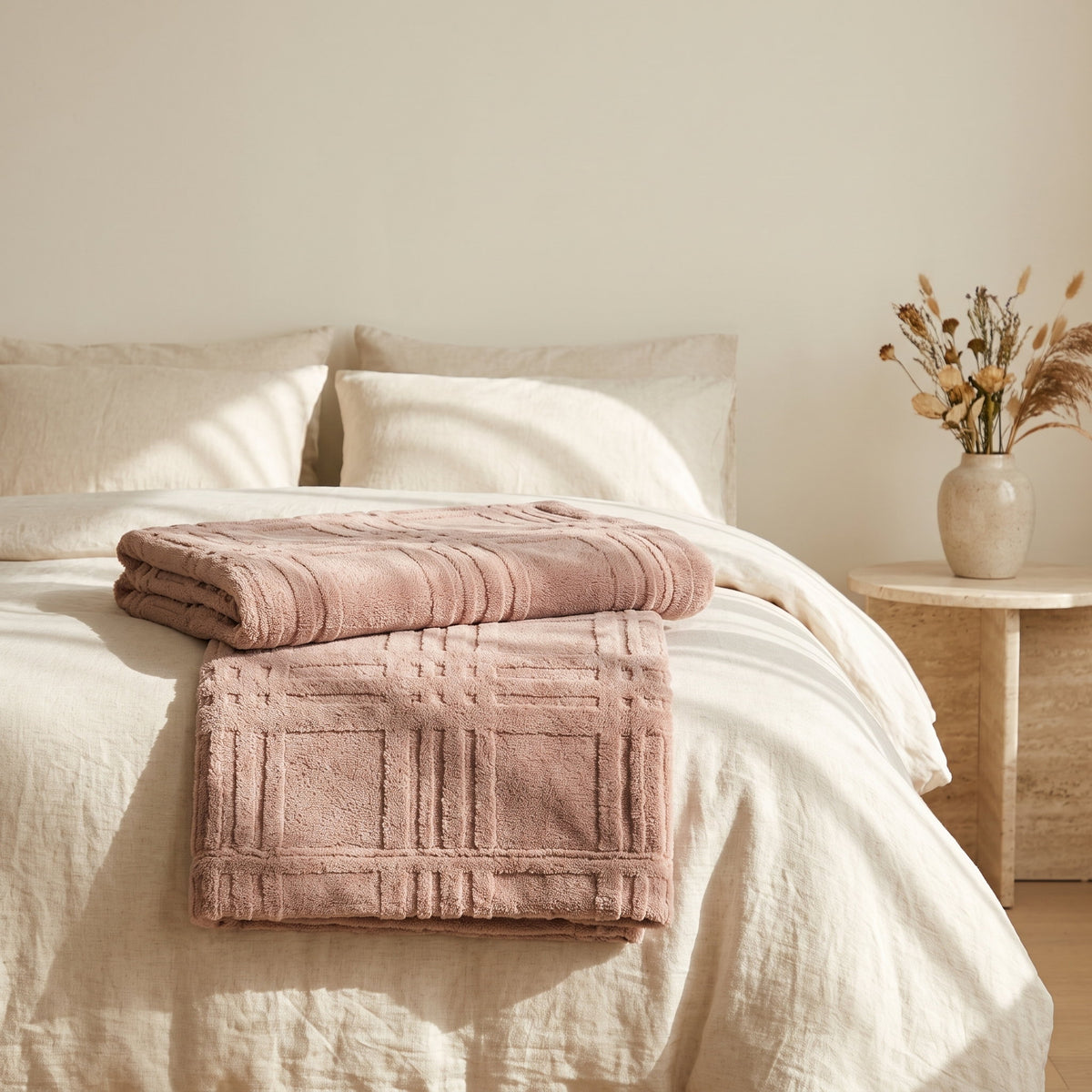 Pavo dusty pink embossed grid blanket folded at the foot of a cream linen bed