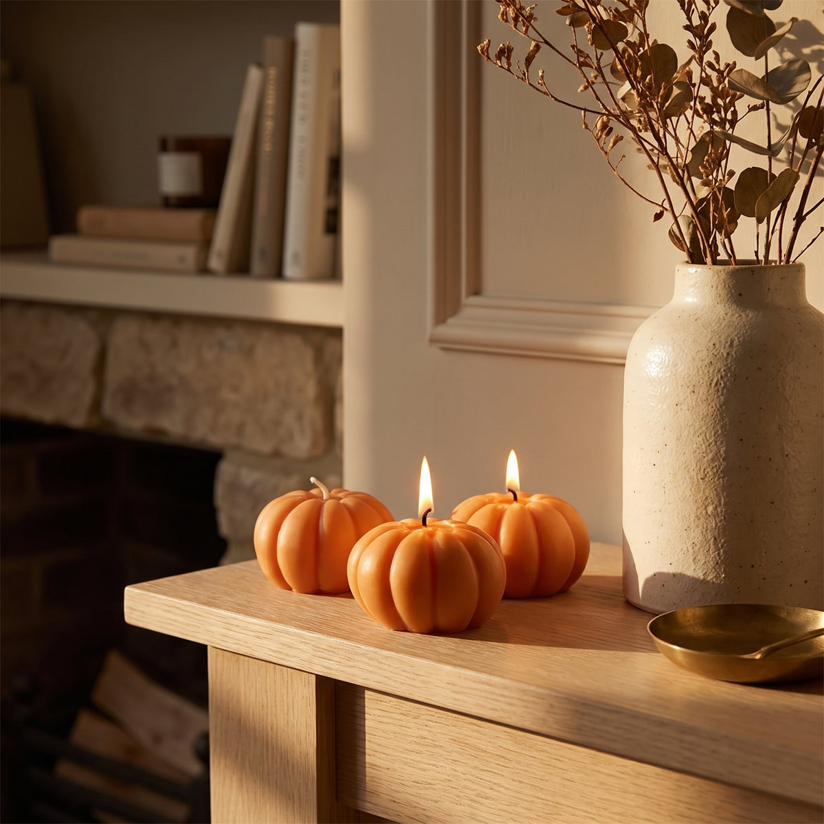 Three Pippin pumpkin candles lit on an oak mantelpiece beside a stoneware vase, Style Room