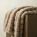 Raven faux-fur throw in off-white draped over a dark wooden block, showing the bobble texture