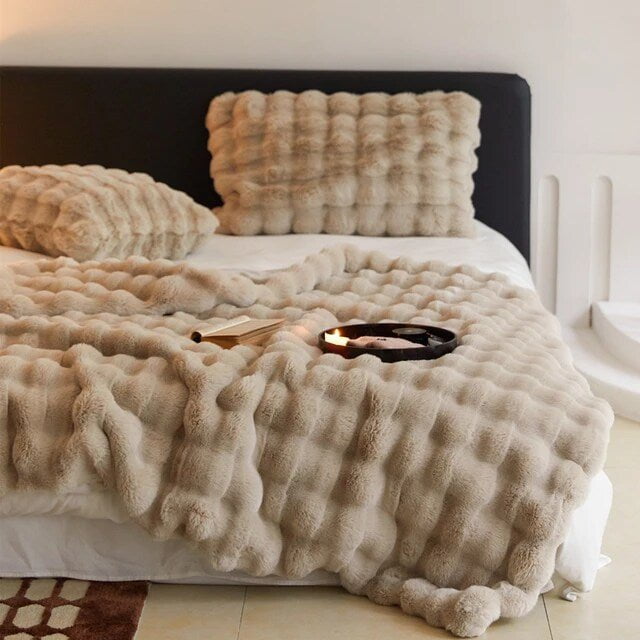 Raven throw and matching cushion in sand on a bed with a dark headboard