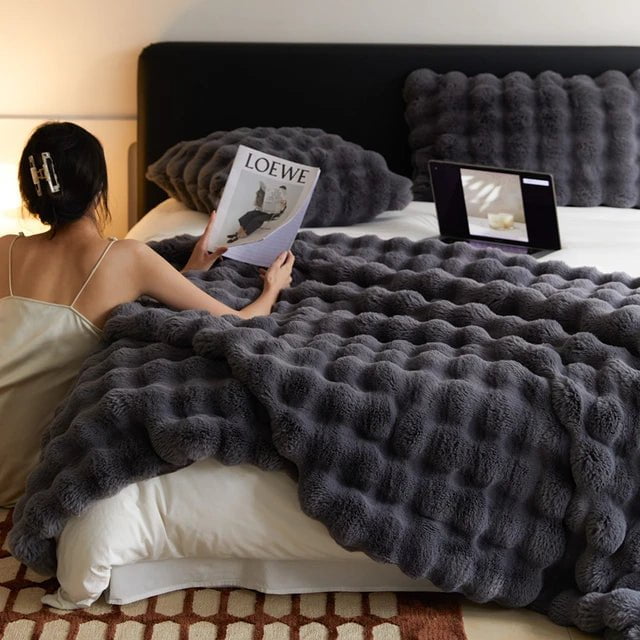 Raven throw and cushion in smoke grey on a bed, with a person reading