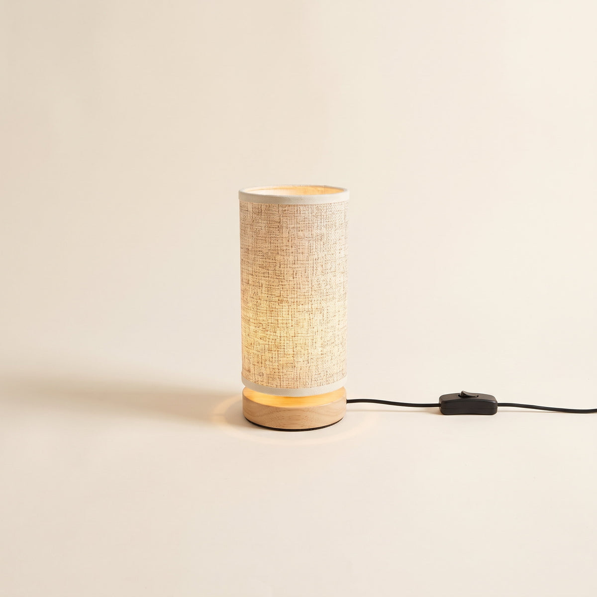 Soren night light with a linen shade on a wood base, lit, with its USB cable, on a cream background, Style Room