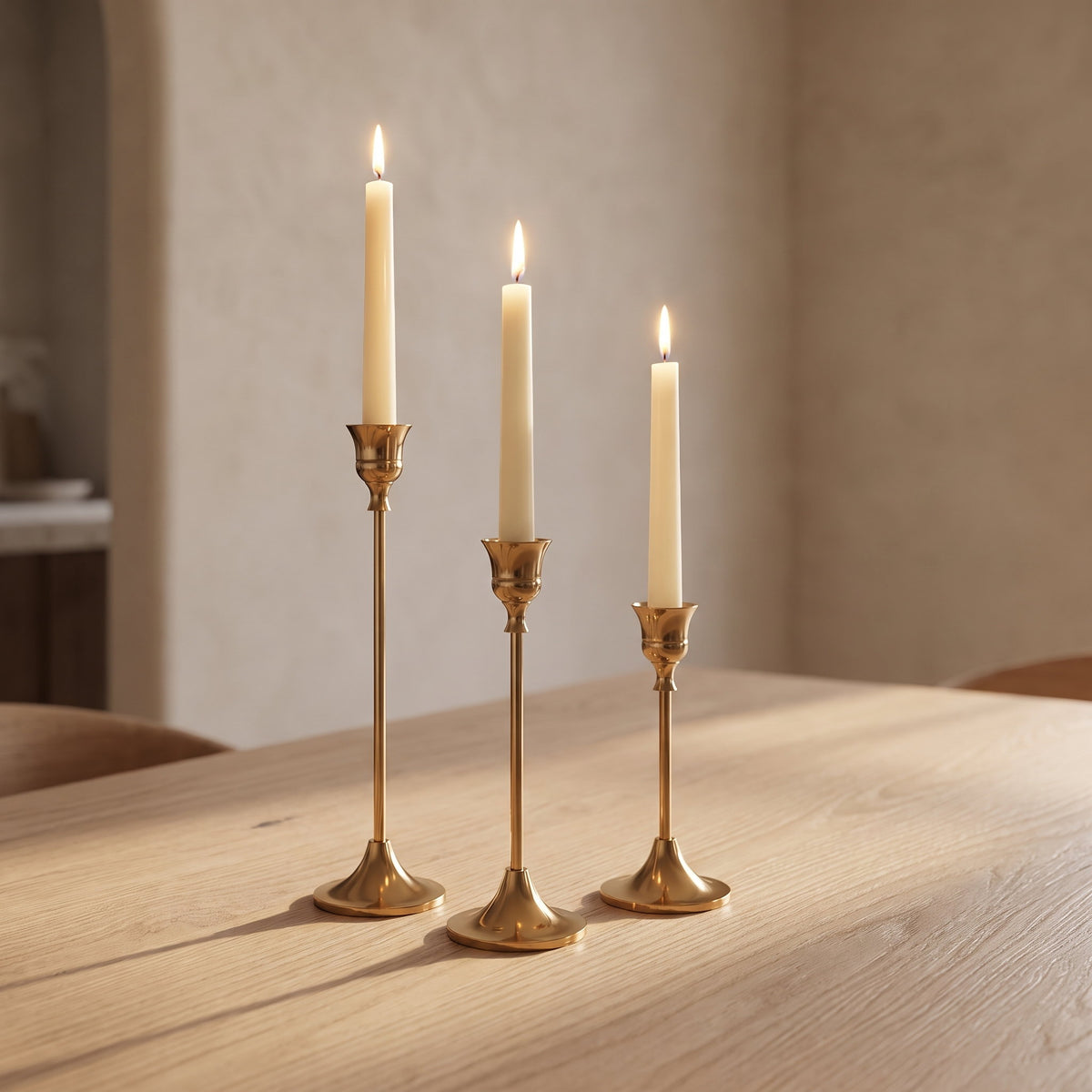 Vero brass candle holders arranged on a pale oak dining table with lit ivory candles